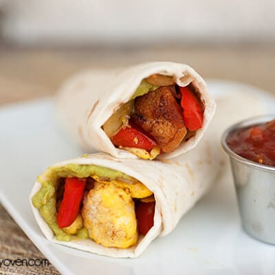 Two burritos on a white plate next to a cup of salsa.