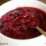 A close up of a cranberry sauce in a white bowl with a spoon in it.