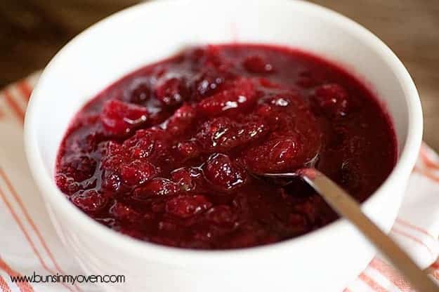A close up of a cranberry sauce in a white bowl with a spoon in it.