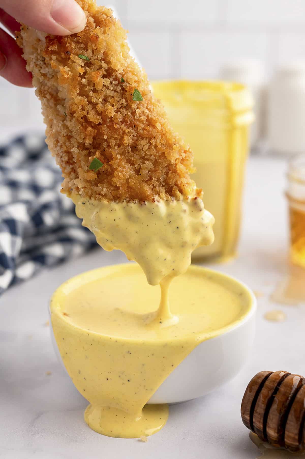 Oven fried chicken tender being dunked in honey mustard dressing.