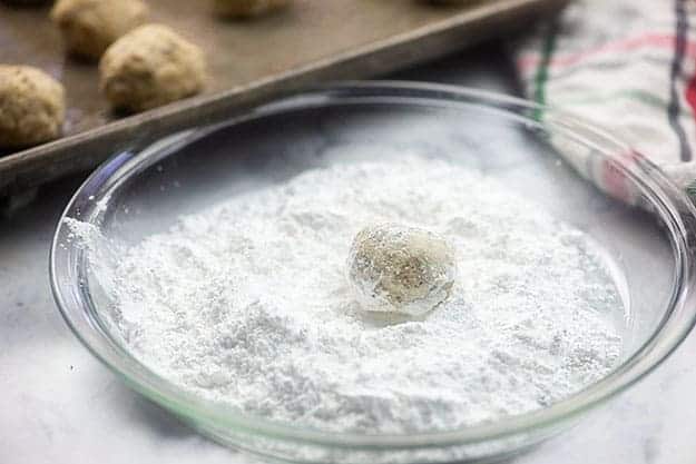 Balled up cookie dough in a pie pan of powdered sugar