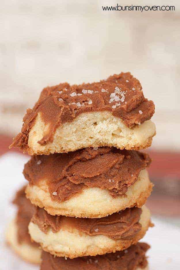 A close up of a shortbread cookie with chocolate icing on a stack of more frosted cookies.
