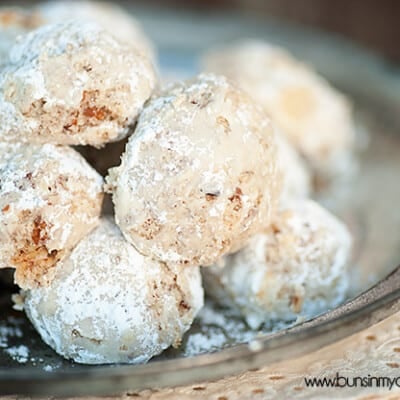 Snowball cookies piled up on a clear glass pie pan.