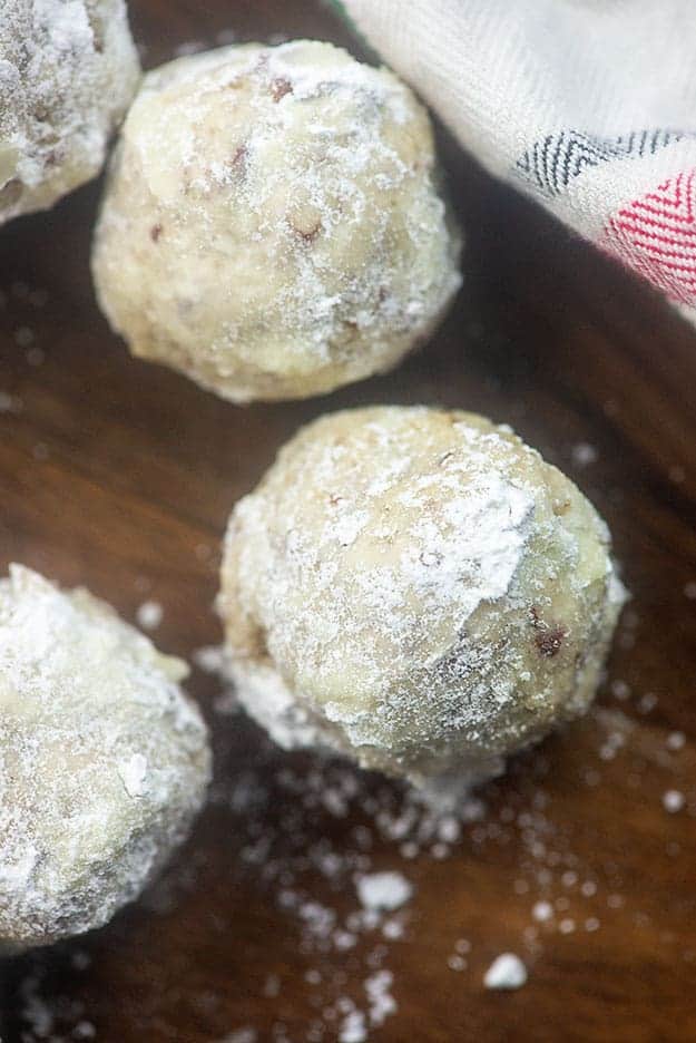 Three snowball cookies on a wooden serving tray.