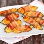 Bacon wrapped jalapeno poppers spread out on a white plate.
