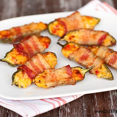 Bacon wrapped jalapeno poppers spread out on a white plate.