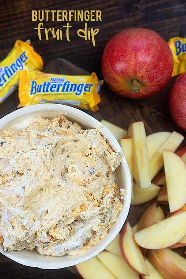 Butterfinger dip in a bowl next to candy bars and apples.