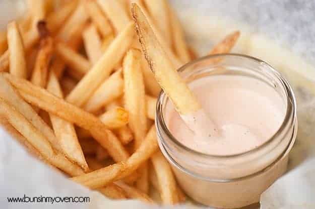 A glass jar of fry sauce surrounded by french fries with a single fry in it.