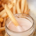 A french fry in a glass jar of fry sauce.