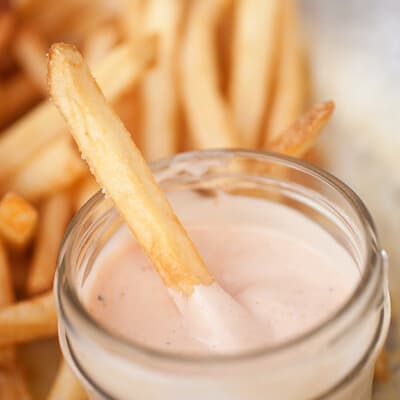 A french fry in a glass jar of fry sauce.