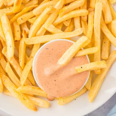 Small white dish of fry sauce surrouonded by french fries.