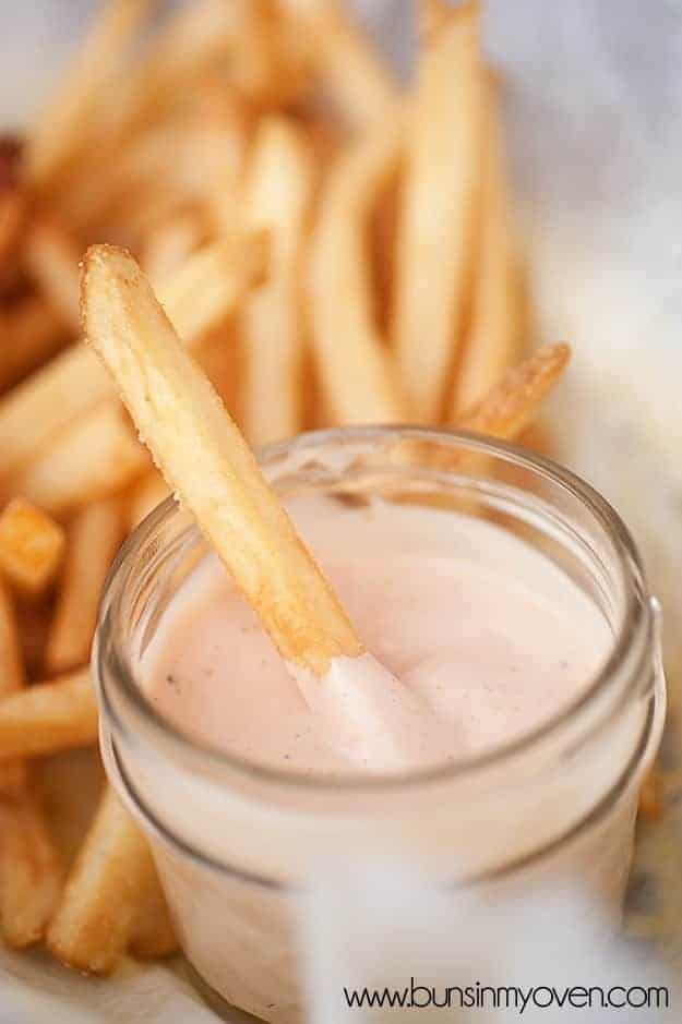 A close up of a french fry in a jar of fry sauce.