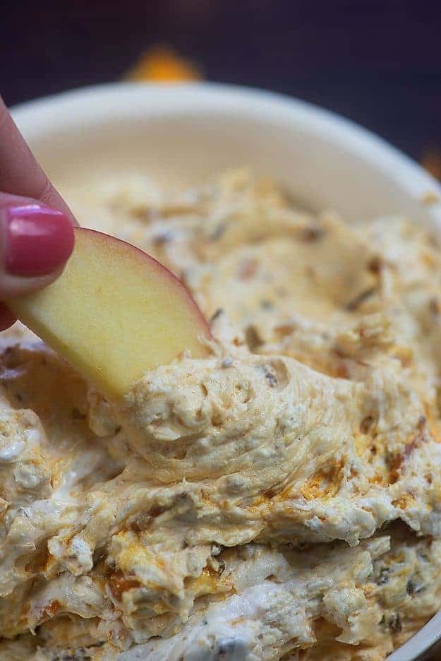 A woman dipping an apple slice into a candy bar dip.