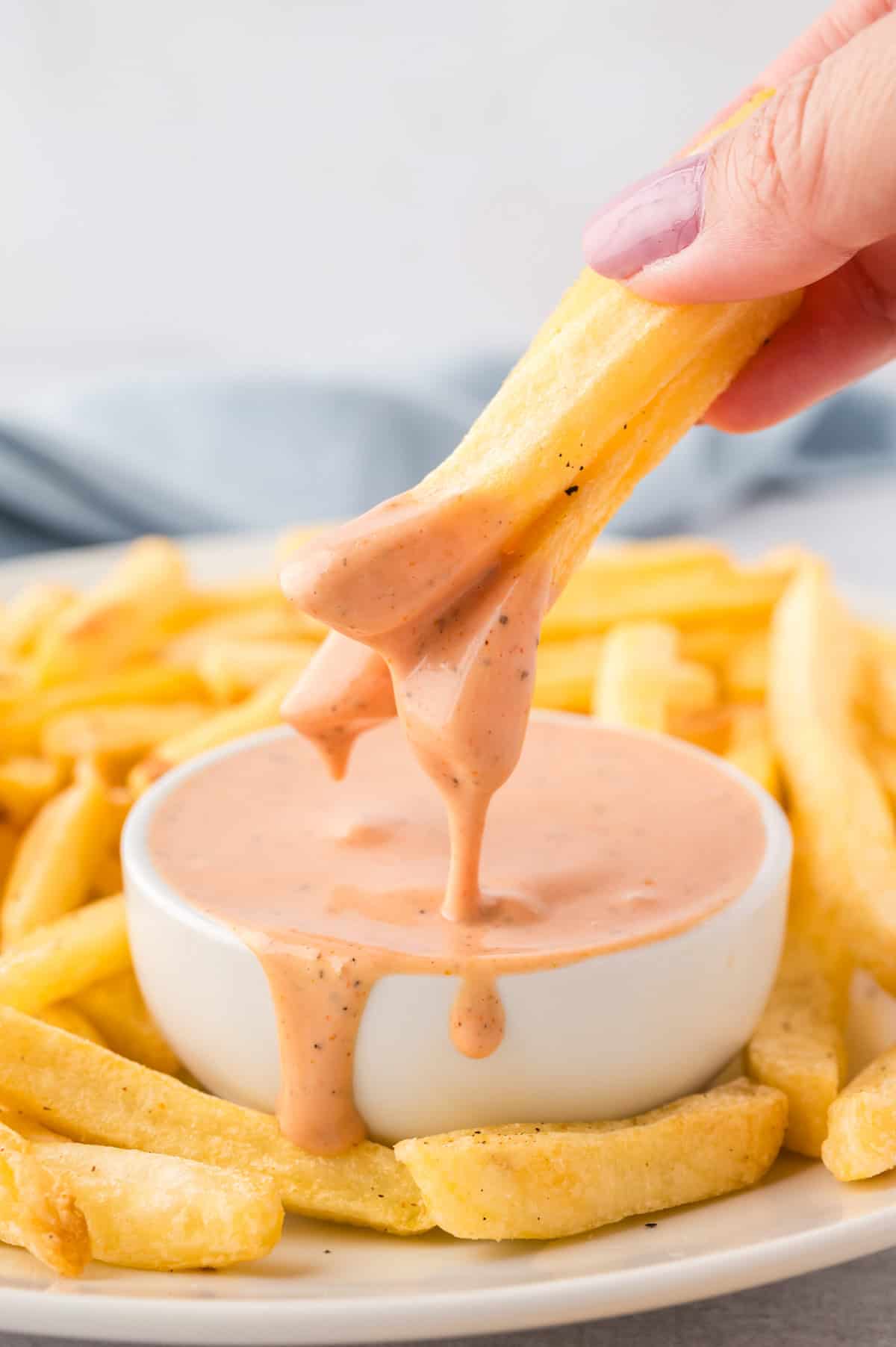 A woman dipping a french fry into a jar of fry sauce.