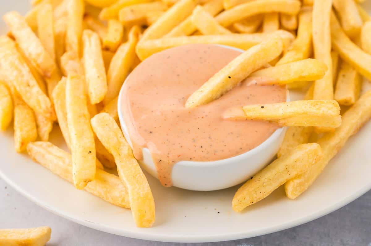 A pile of french fries next to a jar of fry sauce.