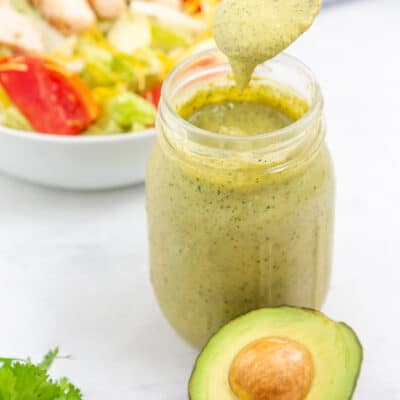 Avocado lime ranch dressing dripping off spoon over jar.
