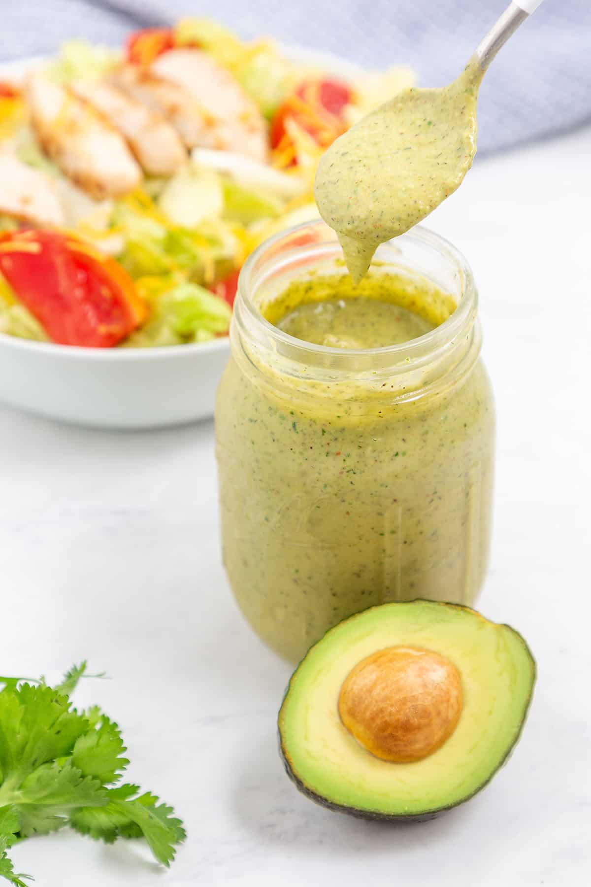 Avocado lime ranch dressing dripping off spoon over jar.