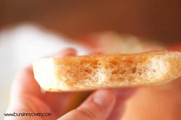 A close up of english muffin with a bite taken out of it held up to the camera.
