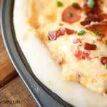 A close up of cheese and bacon pizza in a pizza pan.