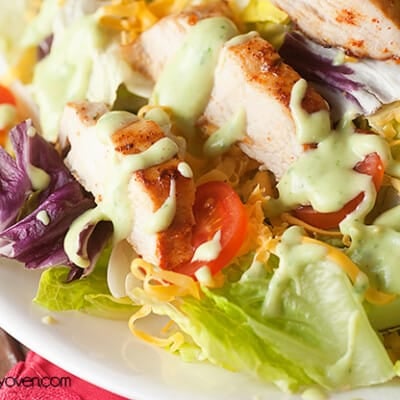 A close up of salad topped with chicken and avocado dressing.