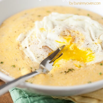 A fork stabbing through a fried egg on top of a bowl of grits.