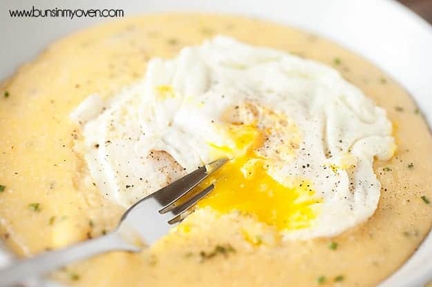 A close up of a fried egg being broken open by a fork on a pile of grits.