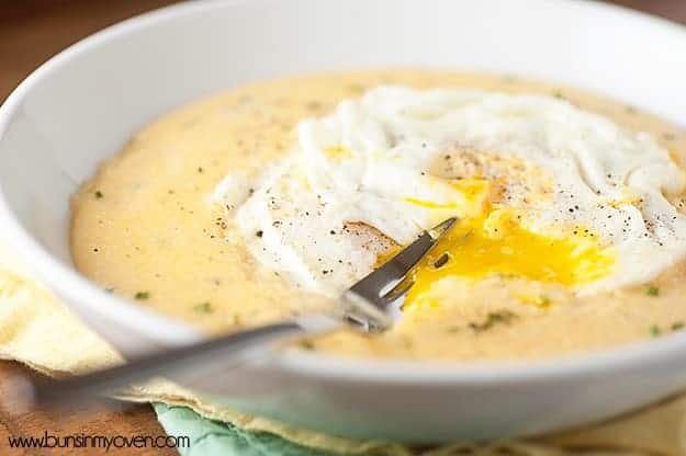 A close up of a fork stabbing through eggs on top of grits.