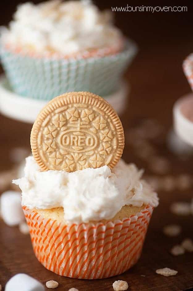 A vanilla oreo resting in icing on a white cupcake.