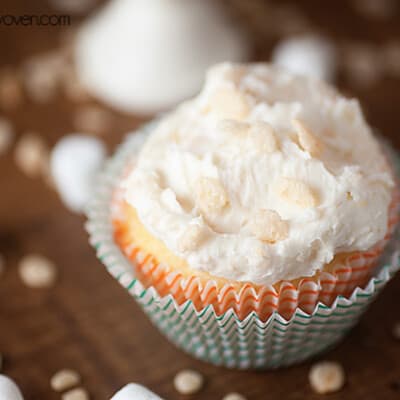 A close up of an iced cupcake with a few paper wraps on the outside of it.