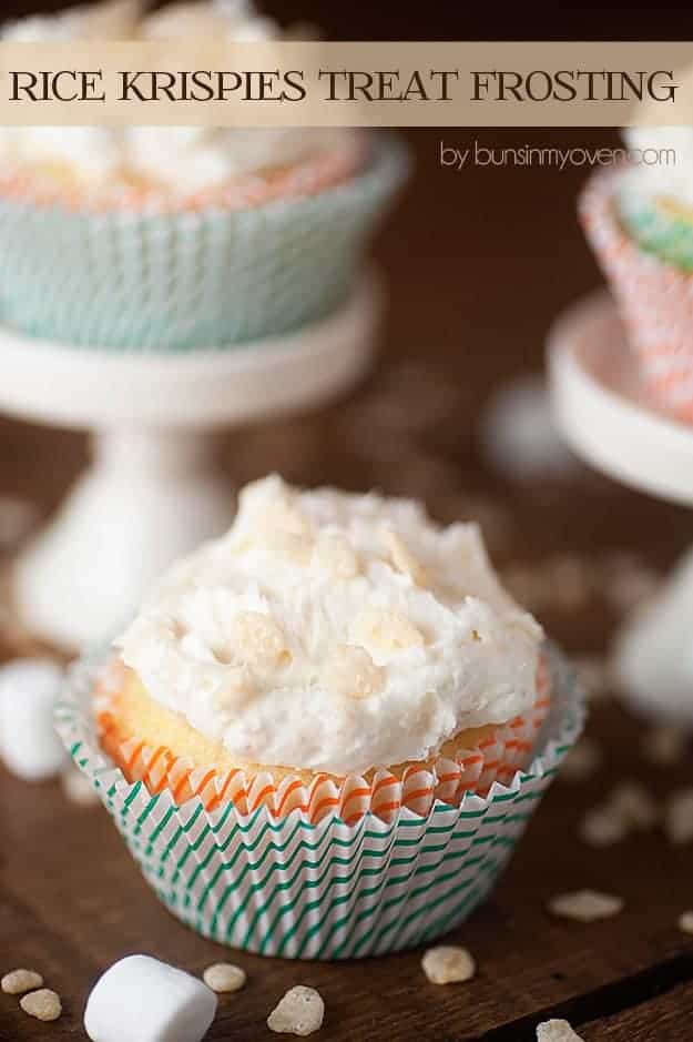 A few paper wrapped cupcakes on a table with cupcakes on stands in the background.