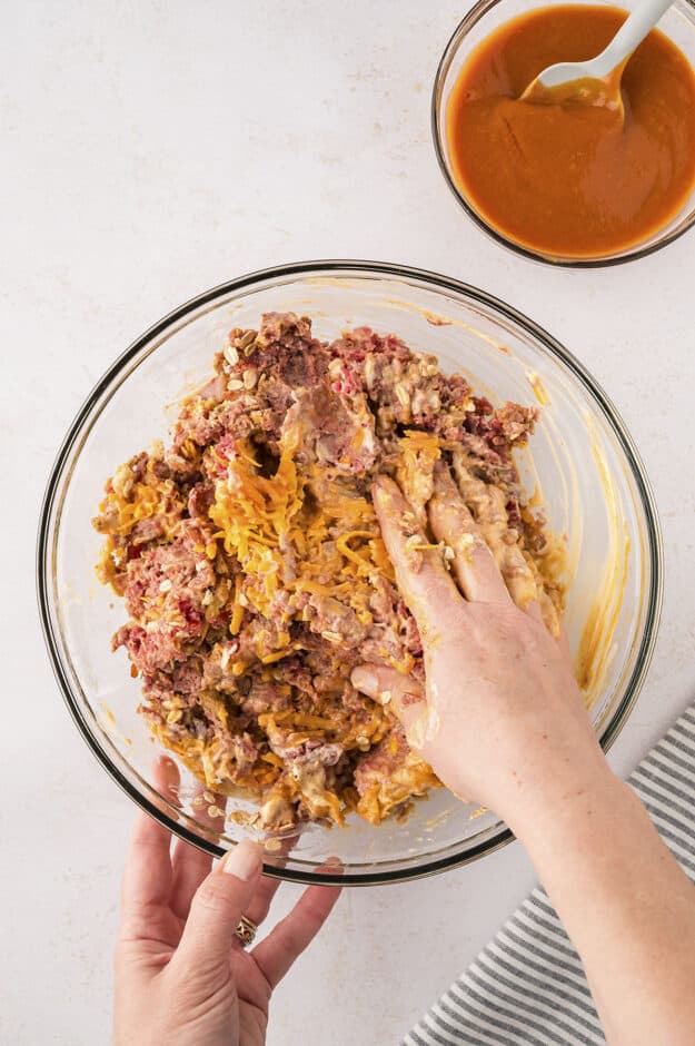 Hand mixing together meatloaf ingredients in bowl.