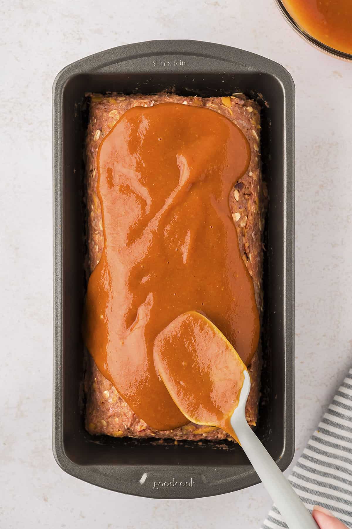 Sauce being spread over bacon cheeseburger meatloaf.