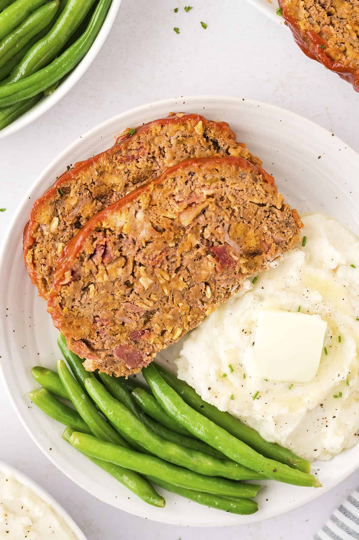 Cheeseburger meatloaf on white plate with green beans and mashed potatoes.