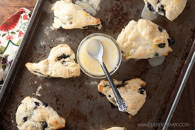 Overhead view of scones and a jar of lemon glaze on a baking sheet.