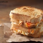 Two grilled cheese sandwiches with buffalo chicken stacked on a paper placemat.