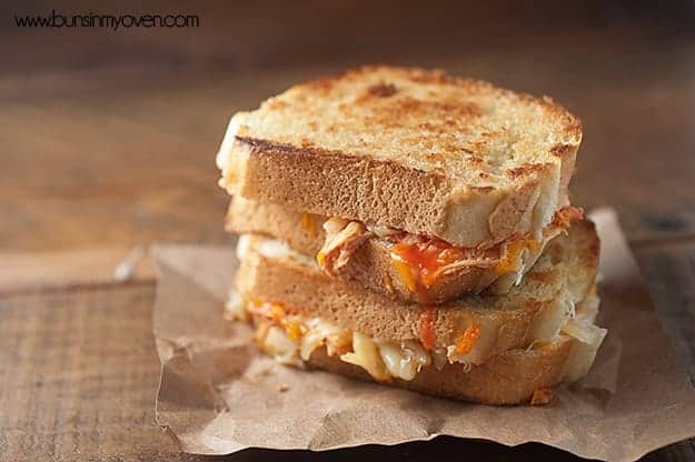 Two grilled cheese sandwiches with buffalo chicken stacked on a paper placemat.