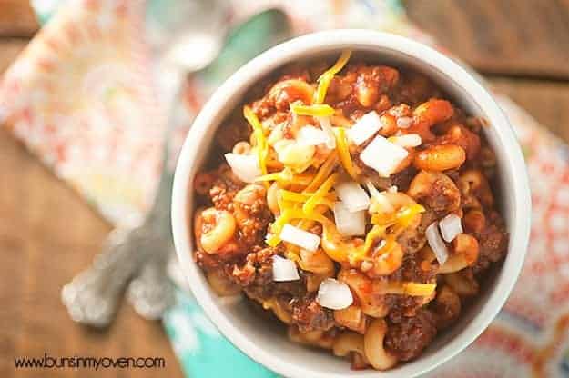 An overhead view of chili mac topped with diced onions in a white soup cup.