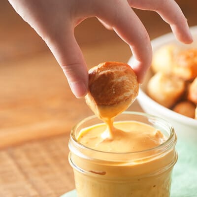A person dipping a pretzel nugget into a jar of cheese sauce.
