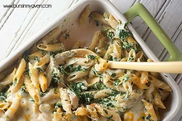 Spinach artichoke dip pasta with a serving removed from the baking dish.