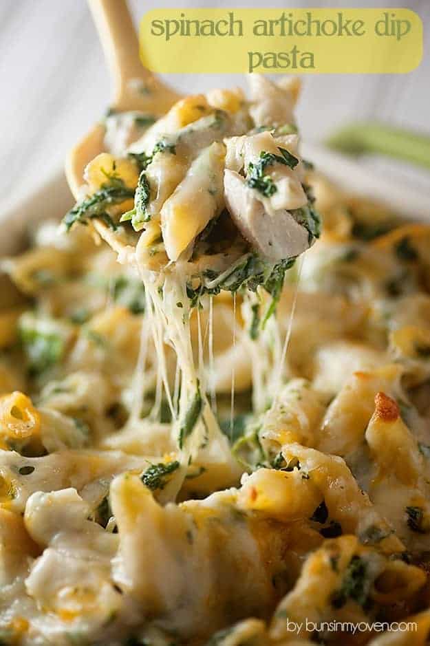 A close up of a wooden spoon holding up a scoop of cheesy chicken artichoke dip to the camera.