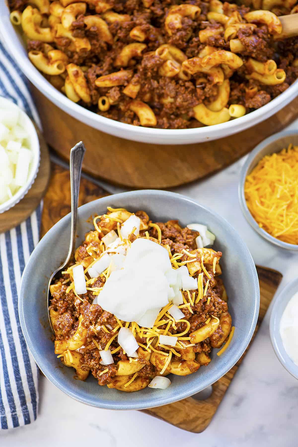 Bowl of chili mac topped with onions and cheese.