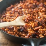 Baked beans being scooped out of a cast-iron skillet.
