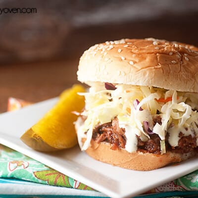 A close up of a sandwich sitting on white plate next to a pickle spear