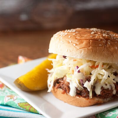 Pulled pork sandwich and a pickle spear on a square plate.