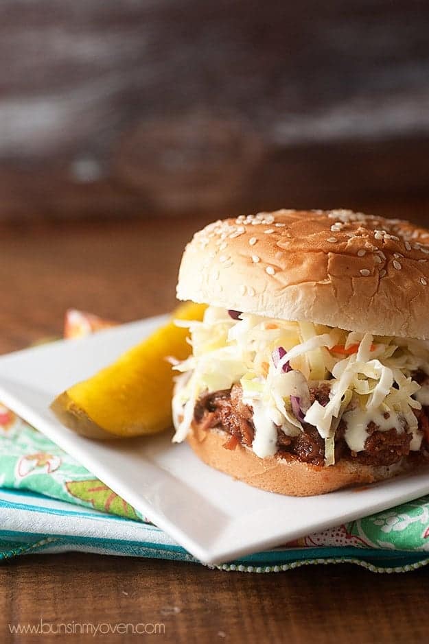 Pulled pork sandwich and a pickle spear on a square plate.