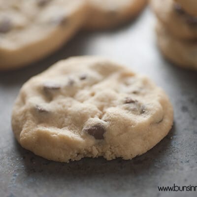 A close up of chocolate chip chookie in the foreground on a baking sheet of cookies.