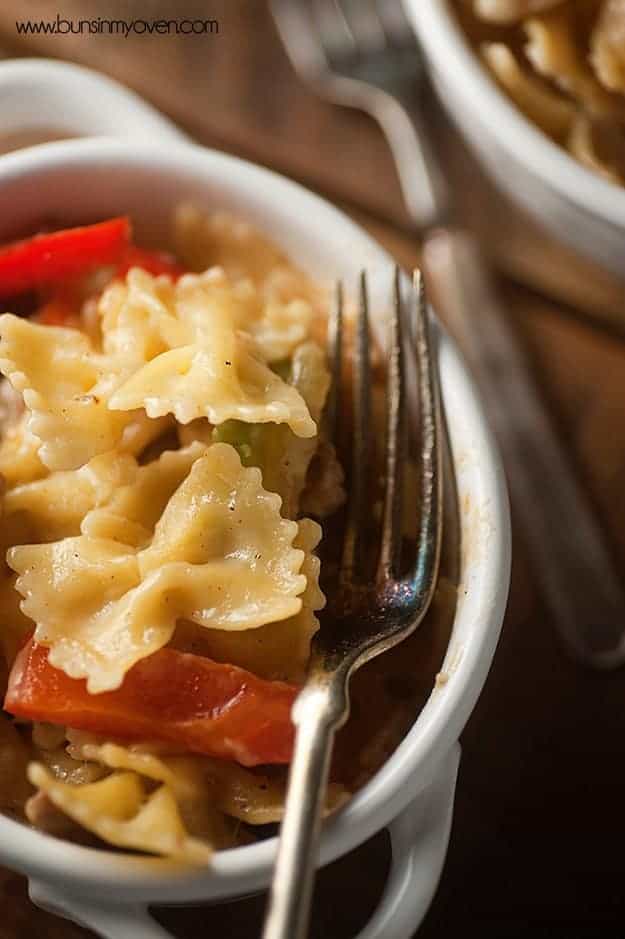 A close up of an overhead view of butterfly pasta with red peppers and slices of steak.