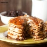 A bite has been cut out of a stack of raisin pancakes on a plate.