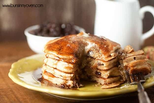 A bite has been cut out of a stack of raisin pancakes on a plate.