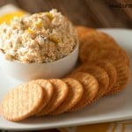 A plate of crackers with a cup of cheese spread.